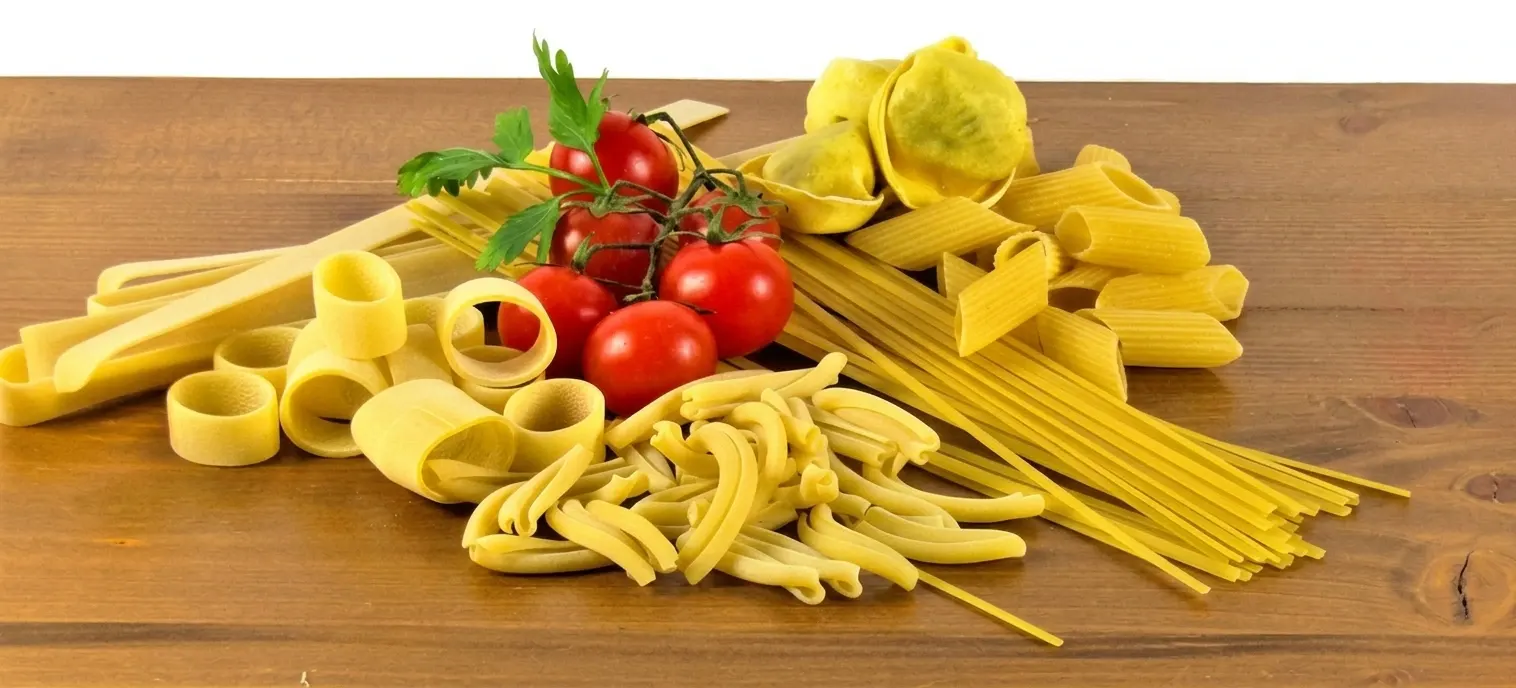 Verse Italiaanse pasta in vele soorten op een houten tafel, met trostomaten en peterselie